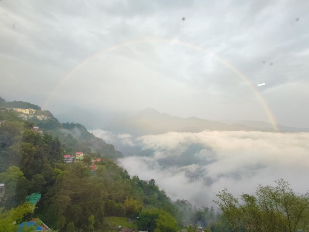 Rainbow arcs over lush green valley with mountains in distance in Sikkim, India
